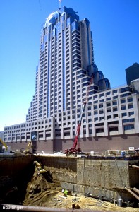 This approximately 70-foot-deep excavation is bounded by existing structures on three sides, including the high rise in the background and Bart on the street side. This side of the excavation exposes the basement walls for the adjacent building.