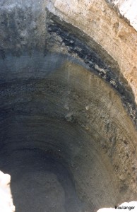 This test pit is located between the above two test pits and towards the side of the valley. An organic soil layer (black) was encountered along with the sand and gravely sand layers. Common borehole sampling techniques with samples obtained at 1.5-m spacings or more could easily have missed this highly compressible layer. Organics are detrimental to roller compacted concrete applications, and thus identifying these layers was important to the project.