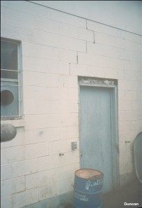 A vertical crack above the door follows the mortar joints in this concrete block wall. Another crack is visible below the window.