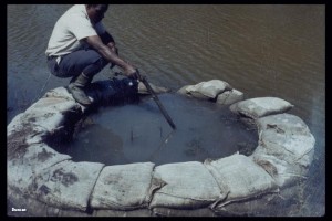 Sand boil due to seepage beneath a levee. A sand bag ring has been built around the boil to slow the outflow and rate of erosion. If the seepage and erosion can't be controlled, the levee will be undermined by progressive erosion and piping.
