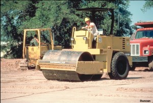 This photo shows a vibratory steel-wheeled roller compacting sand. Vibration is more effective for compacting sands and gravels than static pressure. Water conditioning is not as important for compacting sands and gravels as it is for compacting clays. The total force applied by a vibratory roller is equal to the weight of the roller plus the dynamic vibratory force. (Photo by Caterpillar).
