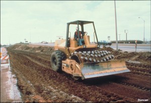 Here a vibratory padded drum roller (similar to a sheepsfoot roller) is compacting clay. The protrusions (pads) on the drum press into the soil when it is loose, and compact the layer from the bottom up. After a few passes, when the fill has been densified to some degree, the roller "walks out," and the entire weight is supported on the pads resting on top of the fill, which results in higher compaction pressures on the soil. (Photo by Caterpillar).