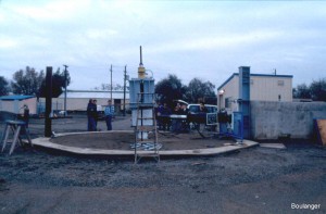 The "test pit" is about 7-m in diameter and 6-m deep below ground. There is a strong beam across the bottom of the pit that provides the reaction for axial loading of the piles. The reaction block for the lateral loading actuator is founded on large-diameter drilled shafts (right side of photo). 