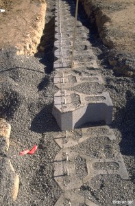 Coarse sand is packed in and around the blocks. The top surfaces of the blocks must be swept free of soil before the next level of blocks can be placed. Dowels are placed in the small-diameter holes in the blocks, and connect the upper blocks to the lower blocks in an overlapping sequence.