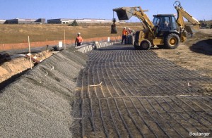 Sheets of geosynthetic "geogrid" are the reinforcement for the soil backfill. The front-end loader was used to place coarse sand / pea gravel directly behind the keystone blocks (left side of photo) to act as a drainage layer.