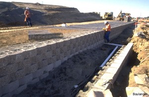 The wall is stepped-back at this location. The white PVC pipes are drain lines that connect to the drainage layer directly behind the blocks.