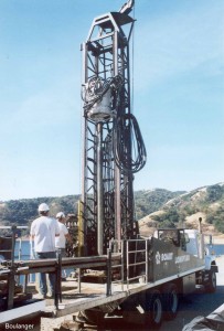 The sampler barrel is mounted to the drill head and ready to begin drilling. The driller operates the vibratory head from the controls to the left of the mast. The driller controls the eccentricity of the rotating masses in the vibratory head and the vibration frequency.