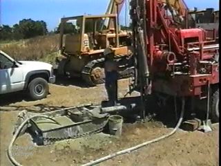 This image shows a rotary wash boring set-up. The drilling "mud," a mixture of water and bentonite, is circulated through the tank in the left-foreground of the photo. The mud is pumped down the drill stem to the hole bottom, where it picks up soil cuttings and carries them to the surface and into the tank. The mud also serves to support the borehole walls. 