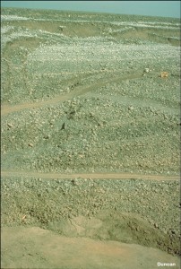 The head scarp and toe bulge are more clearly visible in this photo. Temporary roads have been cut into the slope to provide access for drill rigs. The drill rigs were used to retrieve samples for testing and to install “slope indicators” that were used to measure movements underground.