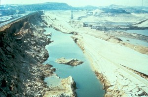 The slide in the upstream shell is shown here with the reservoir emptied. The paved road surface identifies the former crest of the dam.