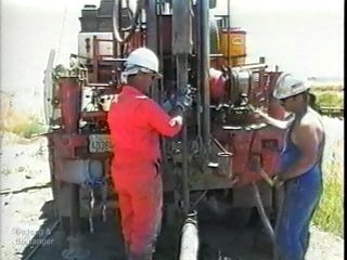 The third main section of the video describes different sampling methods, including SPT sampling, thin-walled tube sampling (Shelby, fixed-piston, Pitcher barrel), and rock coring. This image shows a Standard Penetration Test (SPT) in progress. The driller on the right is pulling the rope tight on the rotating cathead drum, which then lifts the SPT hammer (top-center of image).